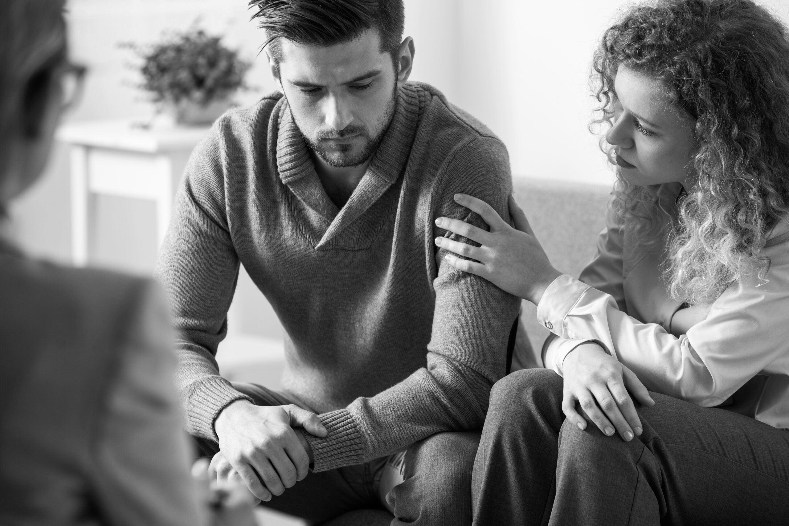 Black and white photo of supportive wife touching husband's arm during psychotherapy session for married people with problems